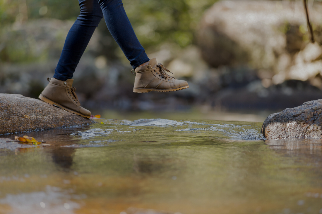 Hiker walking on top of rocks over a river.