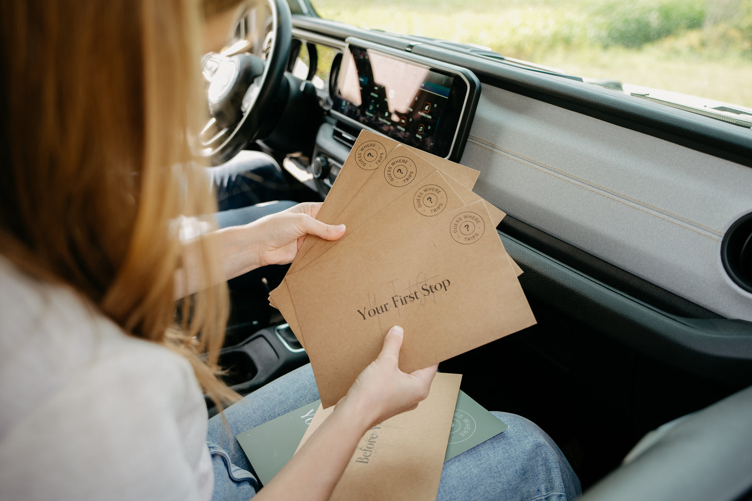 Woman holding four Guess Where Trips envelopes while on road trip