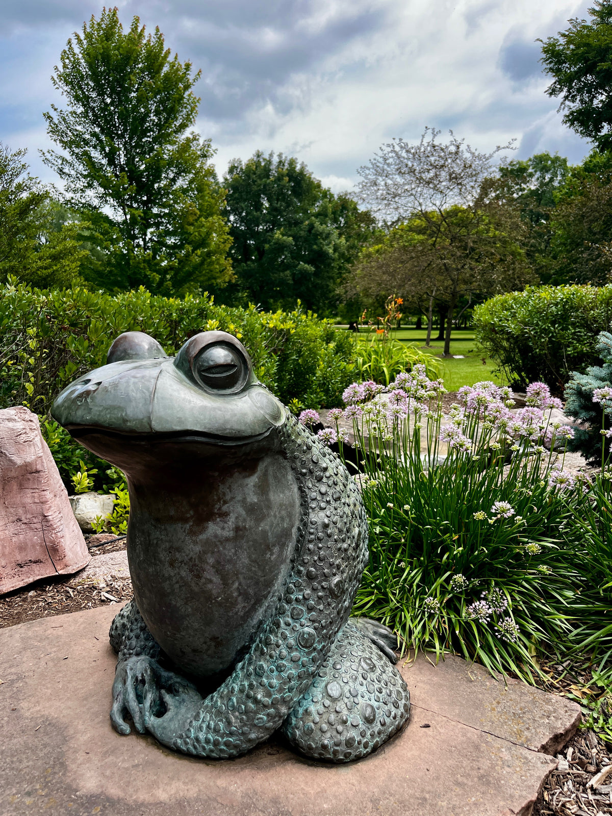 A bronze frog sculpture in a lush garden.