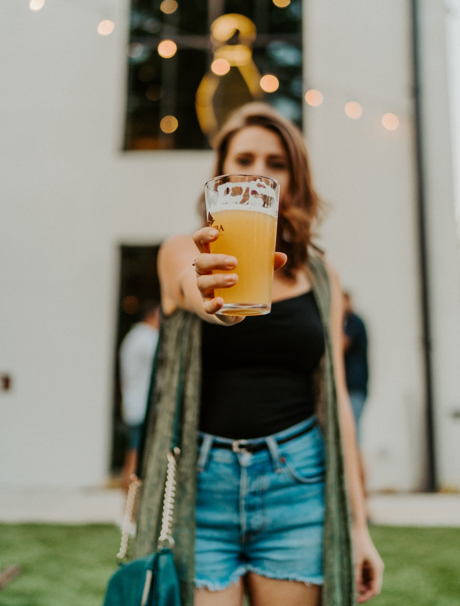 A woman holding up a beer outdoors.