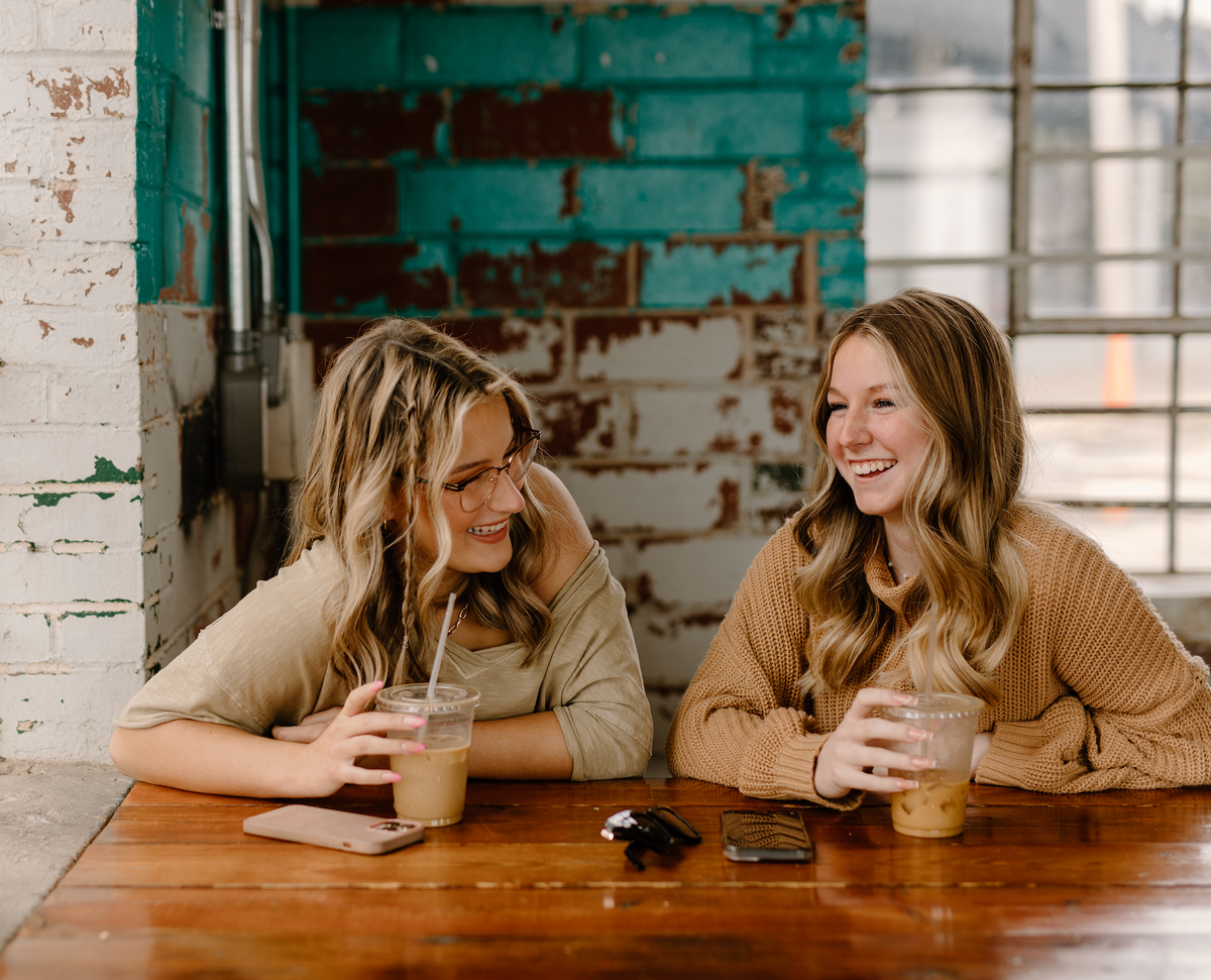 Two women chatting over drinks at a café counter.