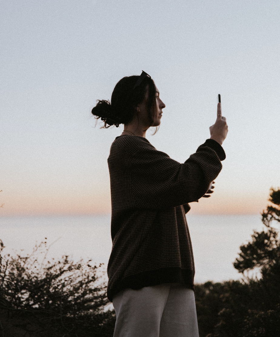 A woman photographing a sunset over the water.