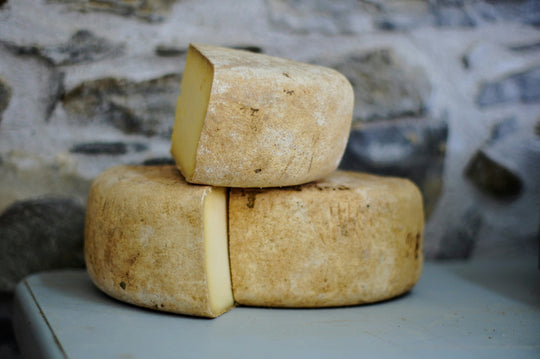 Two stacked cheese wheels on a stone surface with a rustic background