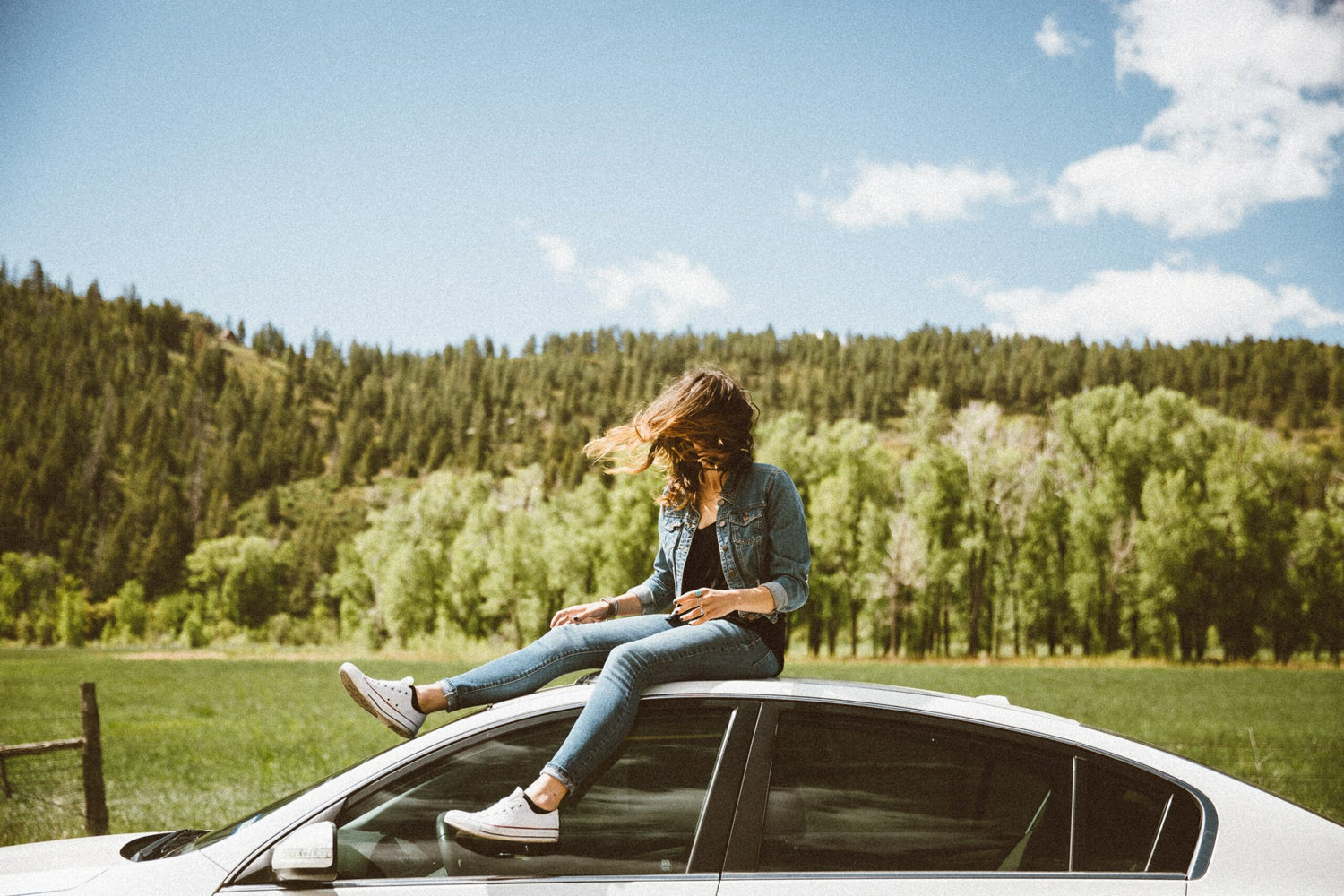 Woman sitting on top of parked car.