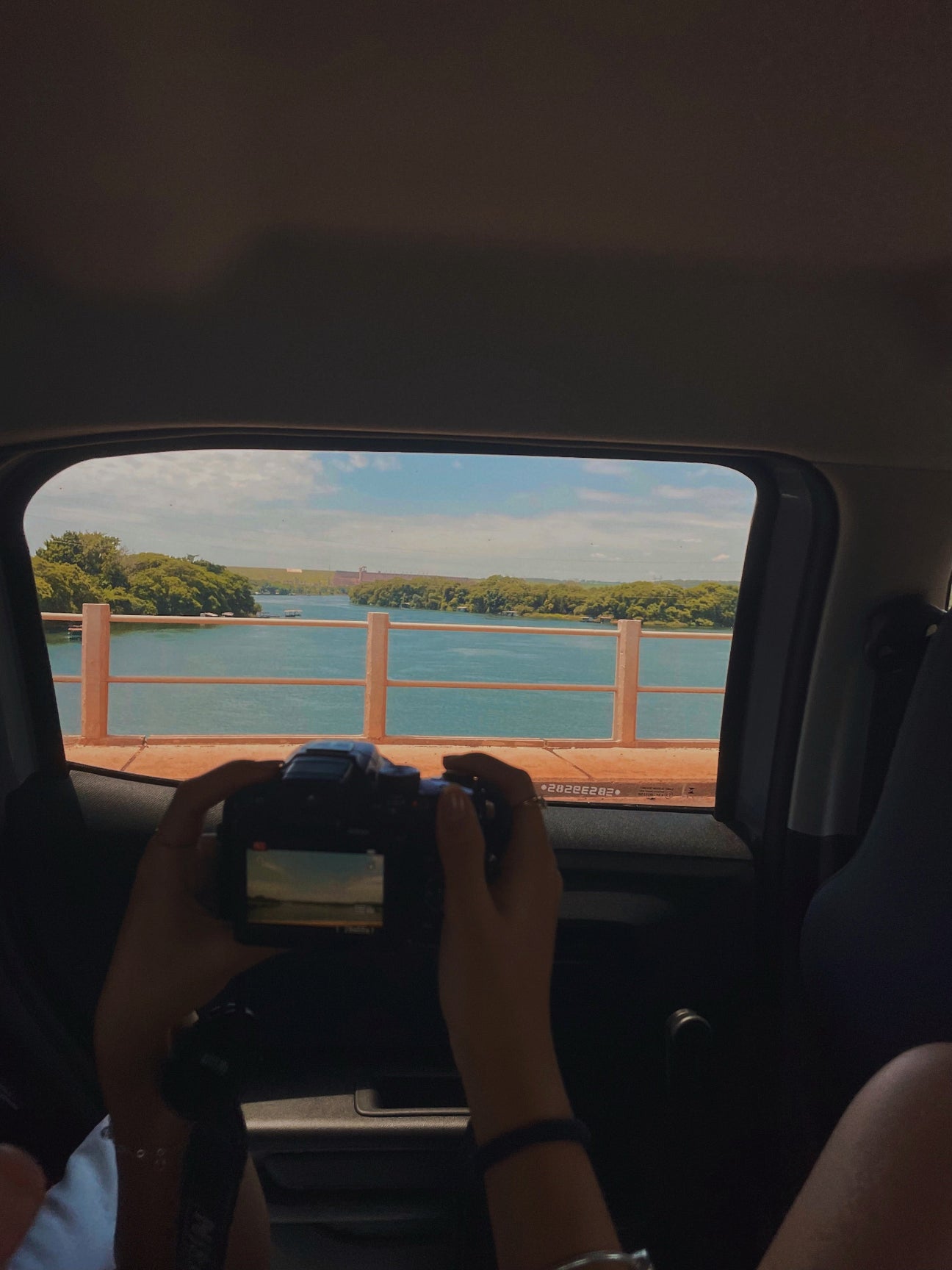 Photographer taking a photo in a car while driving over a bridge over water.