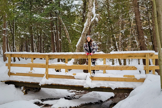 Woman standing on a snowy bridge in the middle of a forest