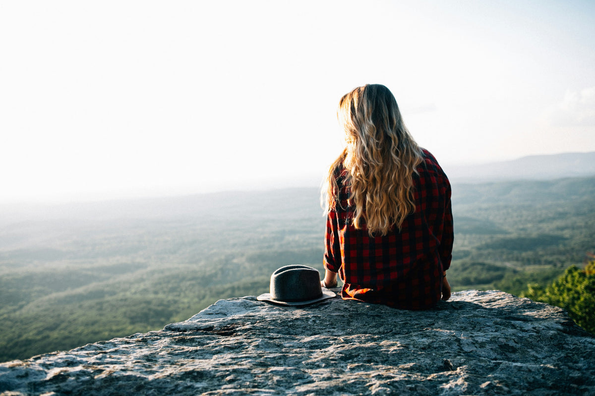 A woman sitting on a rock overlooking a misty valley.
