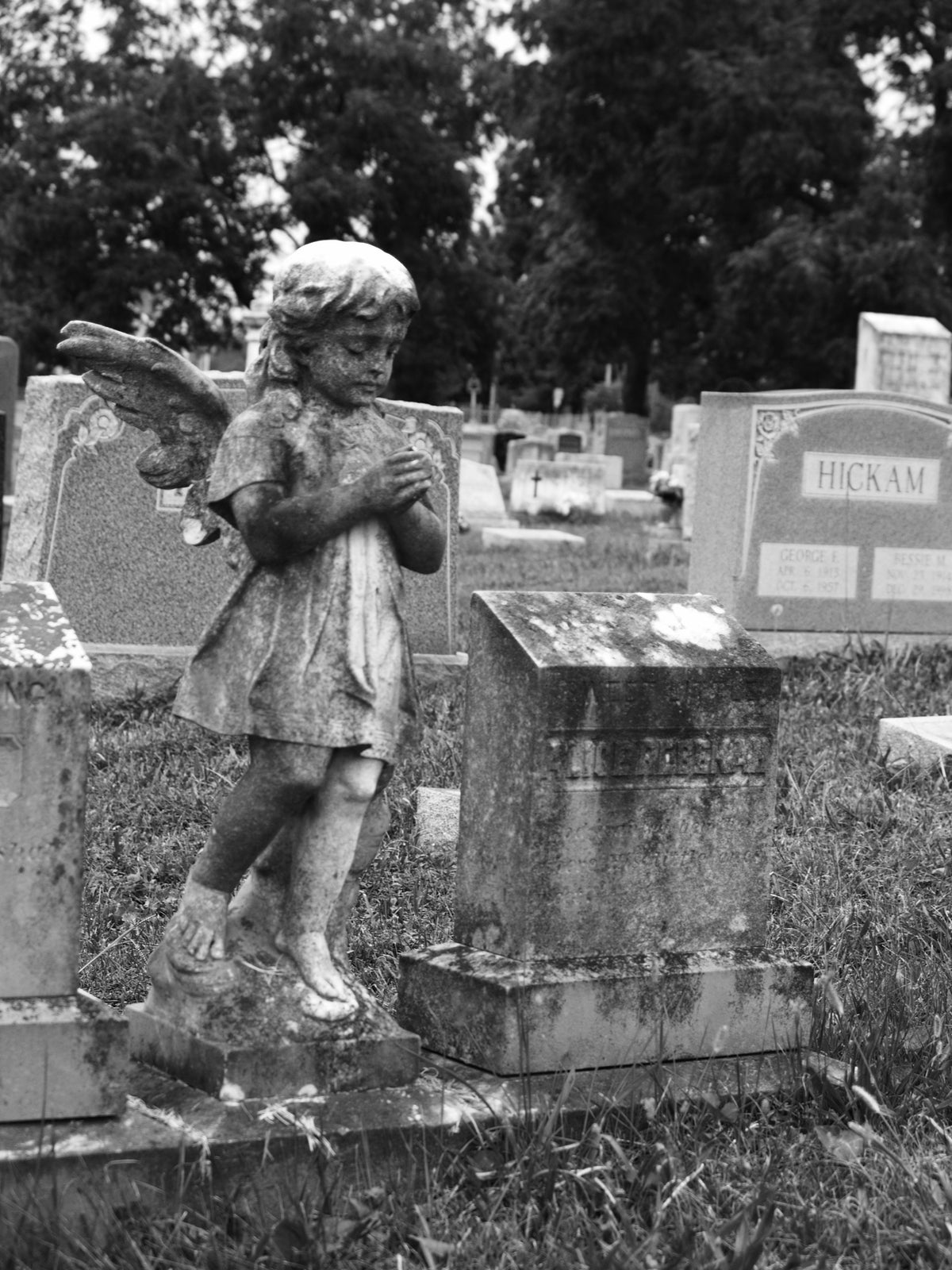 Black and white photo of a stone cherub statue in an old cemetery.