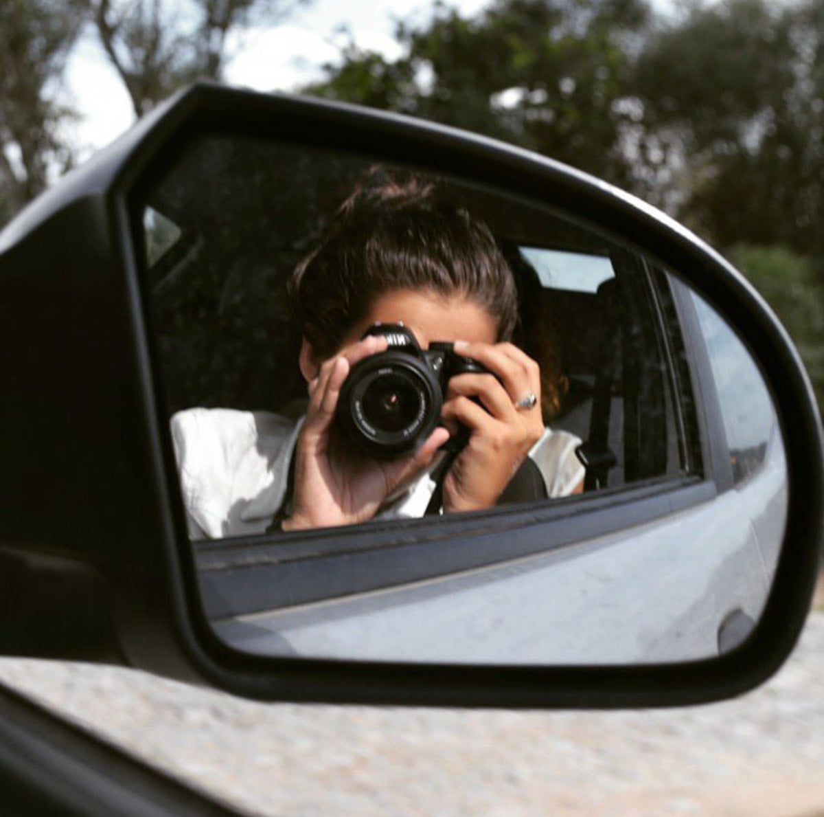 Woman taking a photo of the passenger side mirror in a moving car.