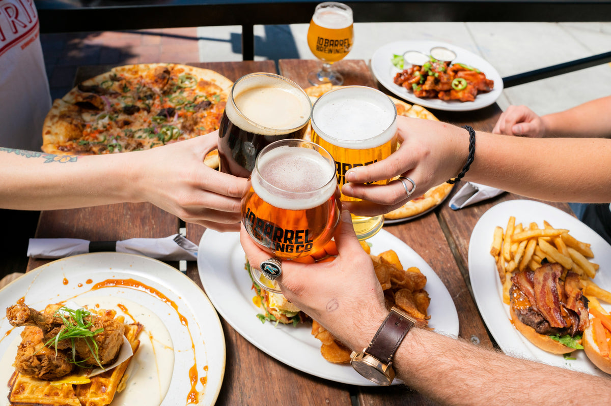 Friends toasting with beers over plates of pasta.