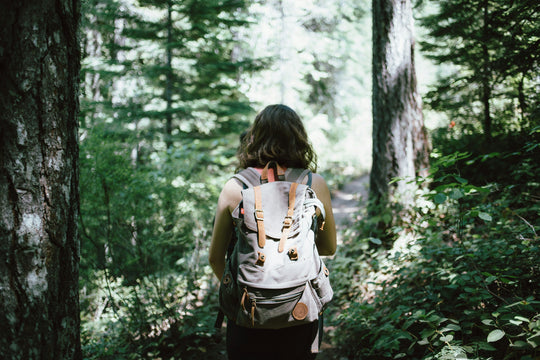Woman with backpack walking along a green forest trail.