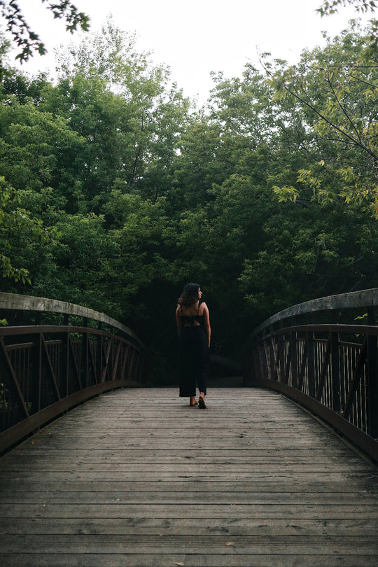 Woman walking along a wooden bridge toward a green forest
