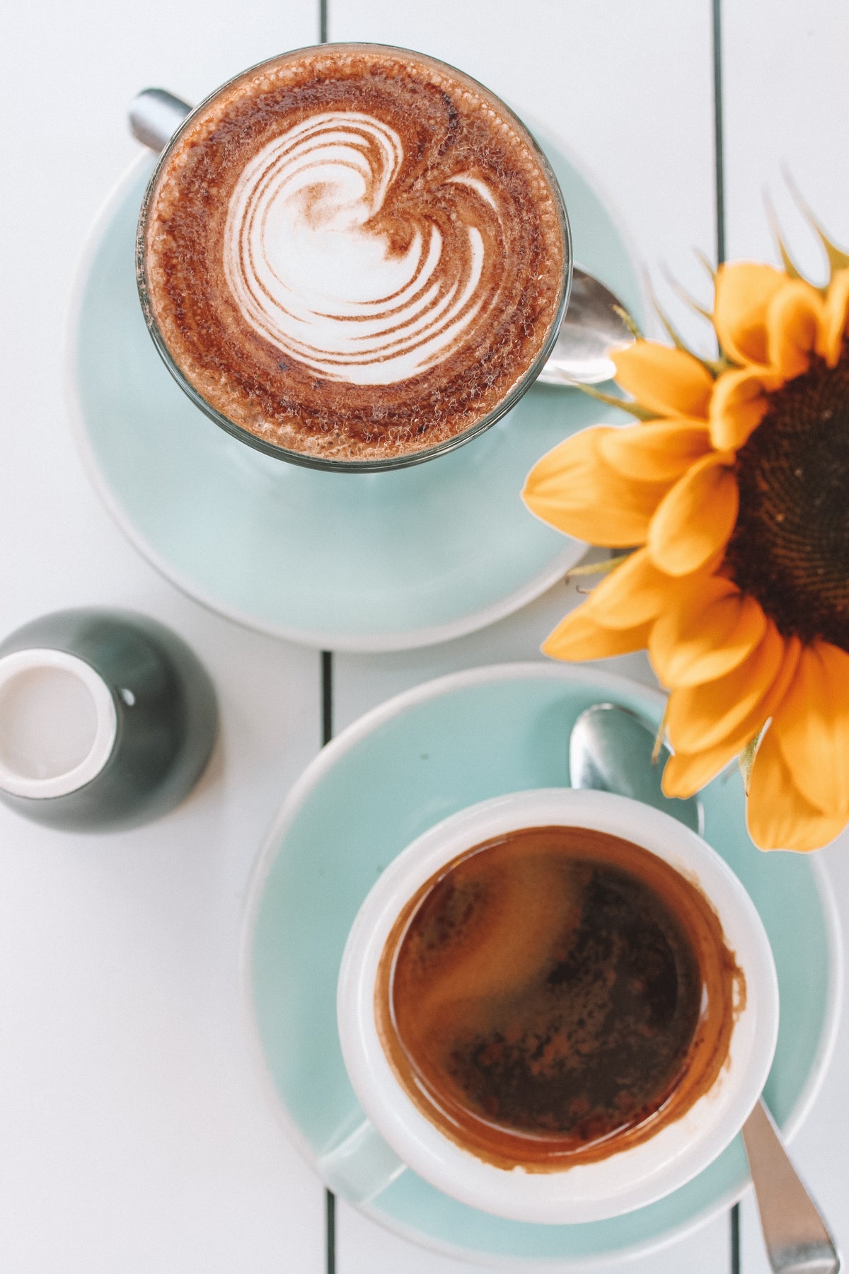 Two lattes beside a sunflower on a café table.