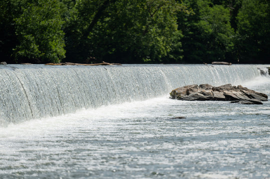 Wide waterfall with green trees above and rocks below.