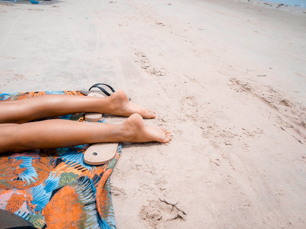 Bare feet on a beach towel in the sand.