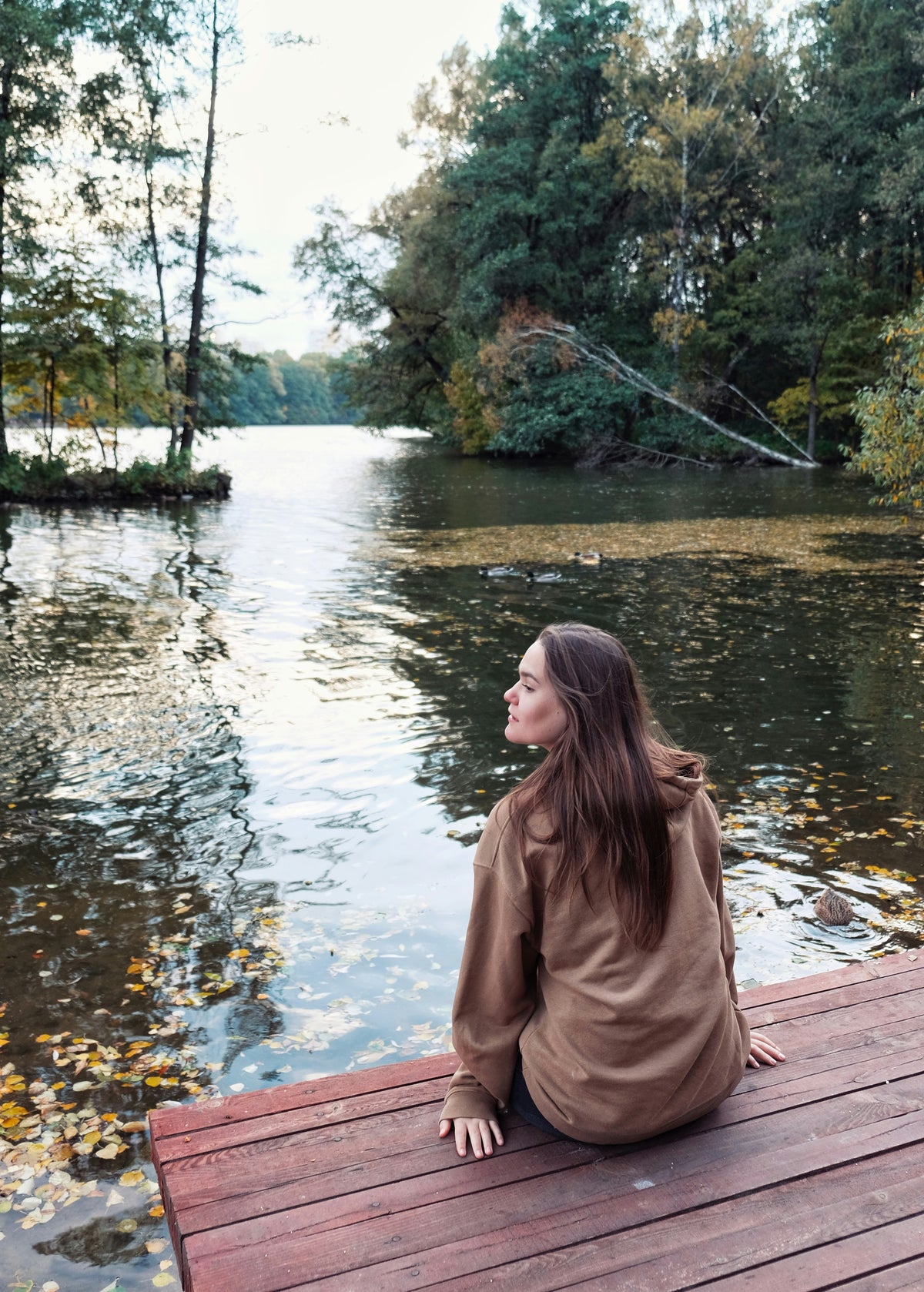 A woman sitting on a dock looking out over a calm river.