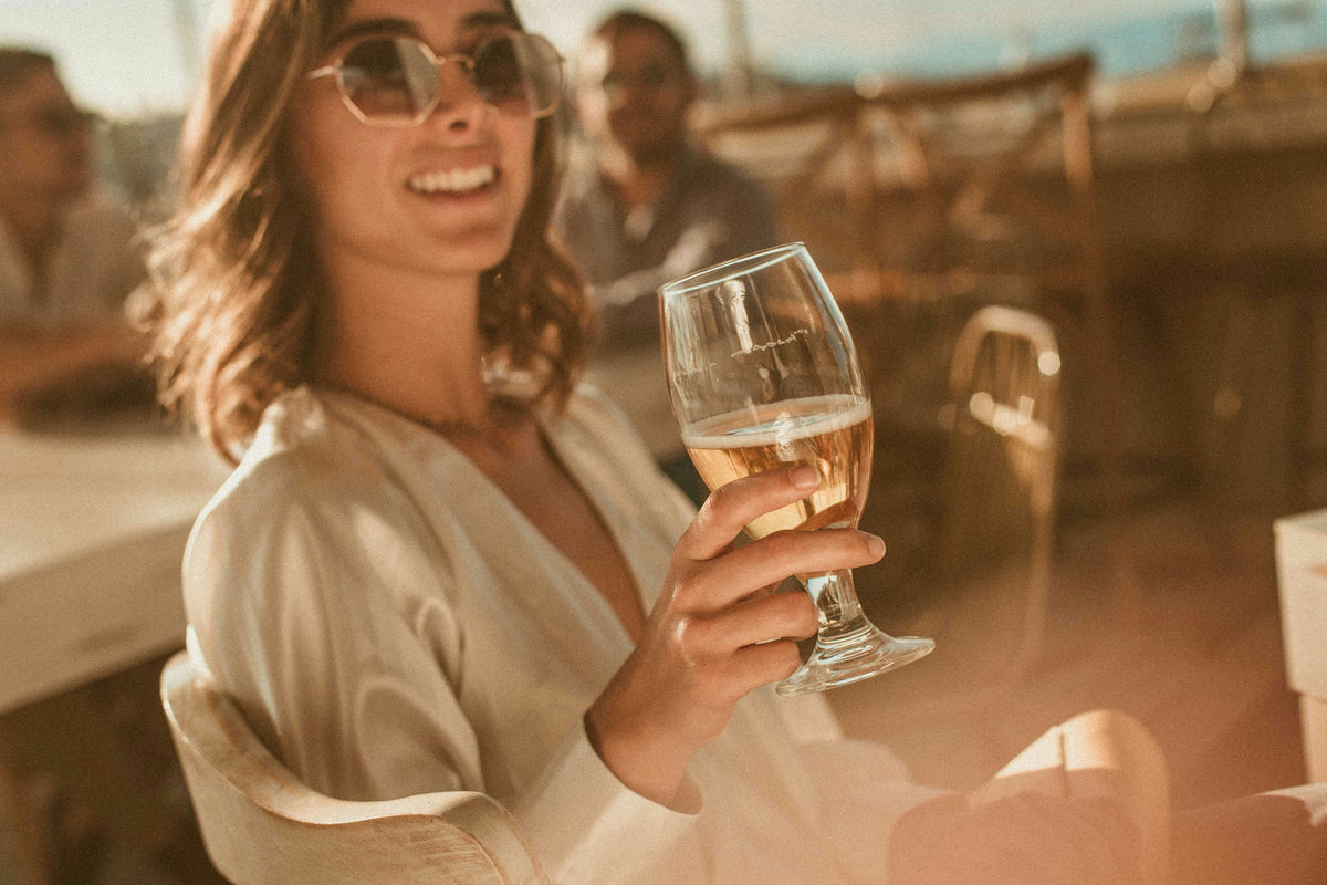 A woman smiling with a glass of white wine.