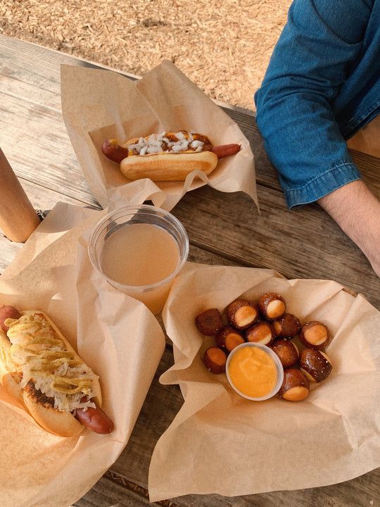 Food spread on a picnic table that includes hot dogs.