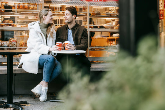 Couple sitting at a cafe table with coffee cups, smiling.