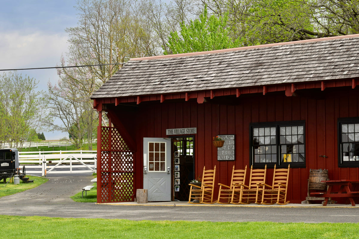 Red barn with rocking chairs and a white door, surrounded by greenery.