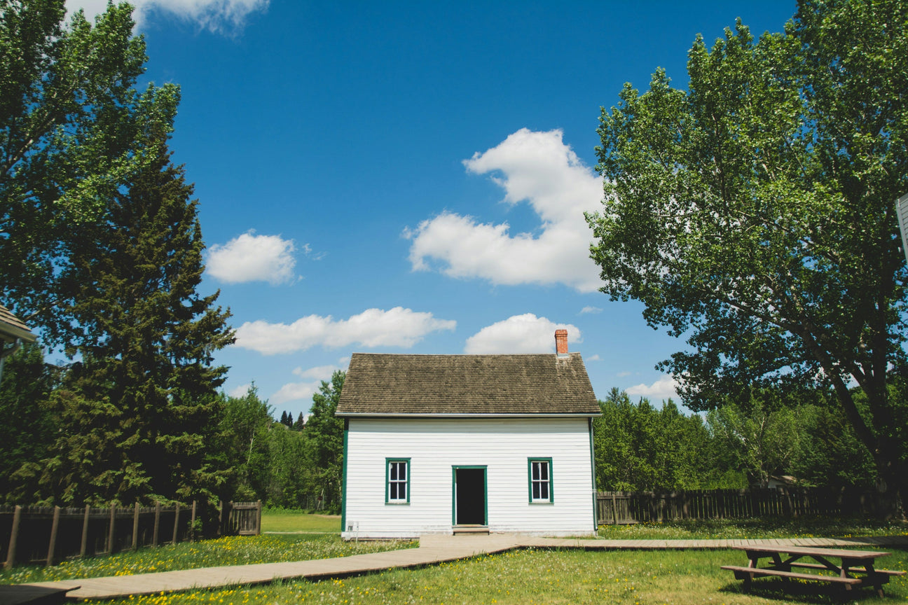 Small white building underneath a blue sky surrounded by trees.