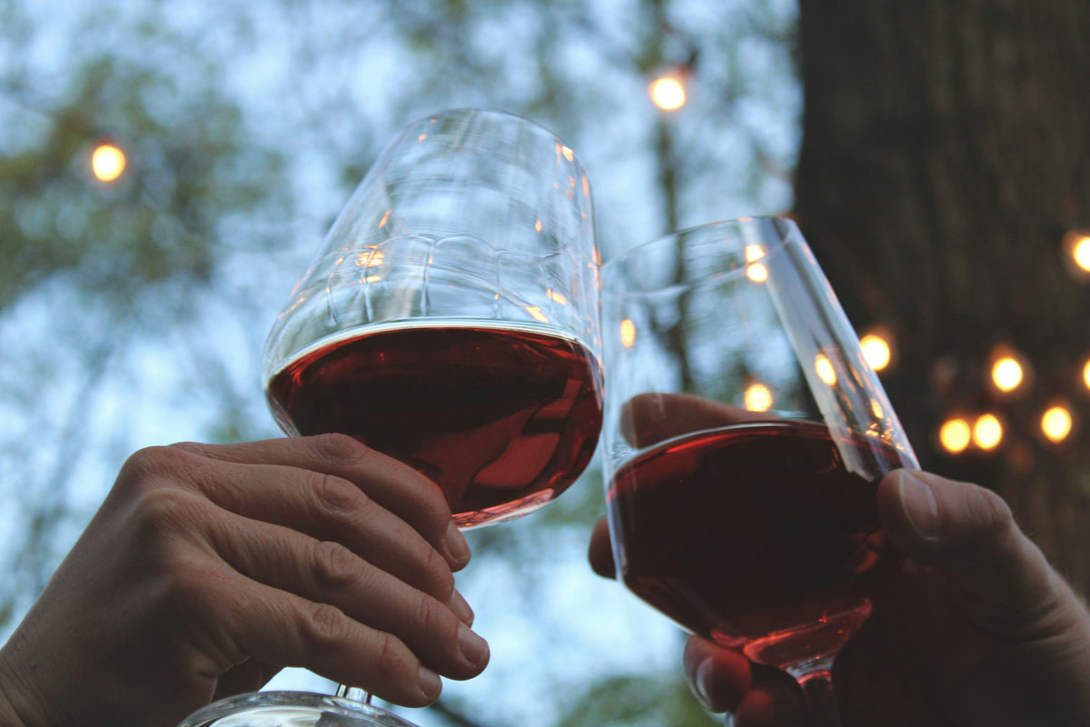 Two people clinking glasses of red wine.