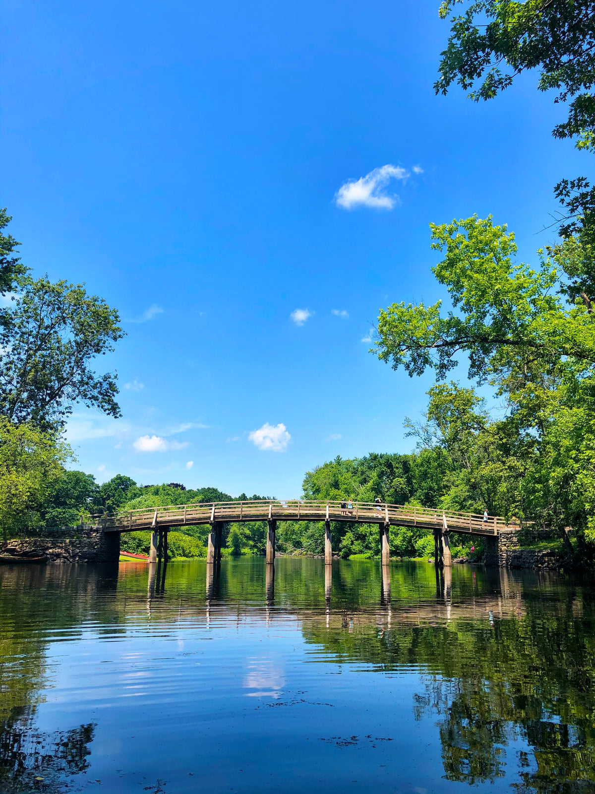 A stone bridge over a calm river under a blue sky.