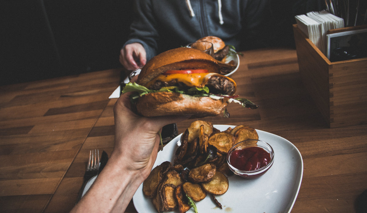 Photo of a woman holding a cheeseburger above a plate of potatoes and ketchup.