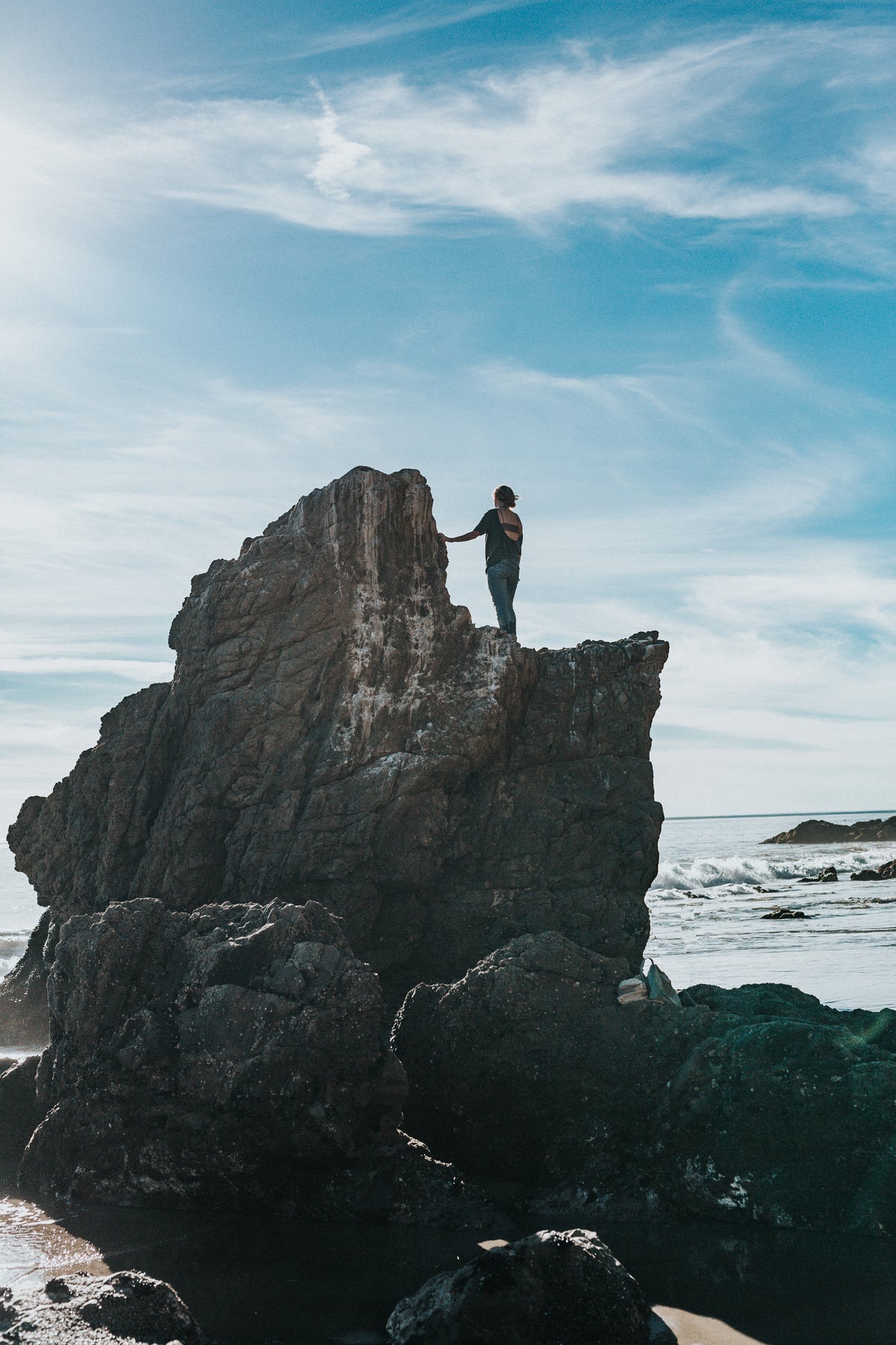 A person standing on top of a rocky sea stack.