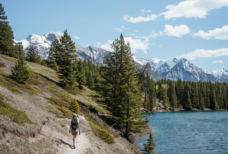 A hiker on a trail beside a mountain lake.