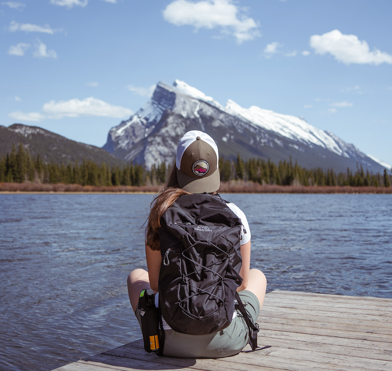 A hiker sitting on a dock looking at a snow-capped mountain.