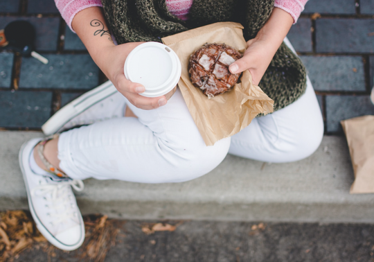 Woman holding onto a takeaway coffee cup and a baked good.