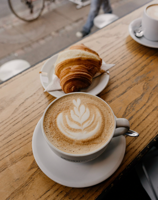 Table at a cafe with a cappuccino and a croissant.