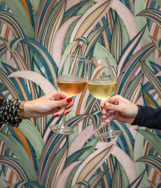 Two people clinking wine glasses in front of a wall mural.