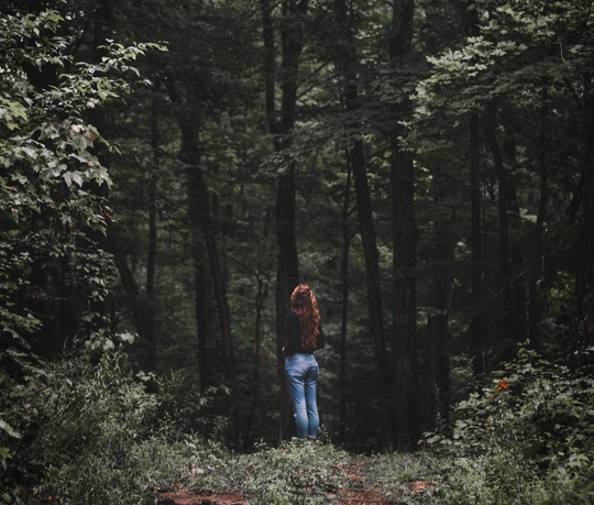 Woman with red hair standing in front of a dark forest.