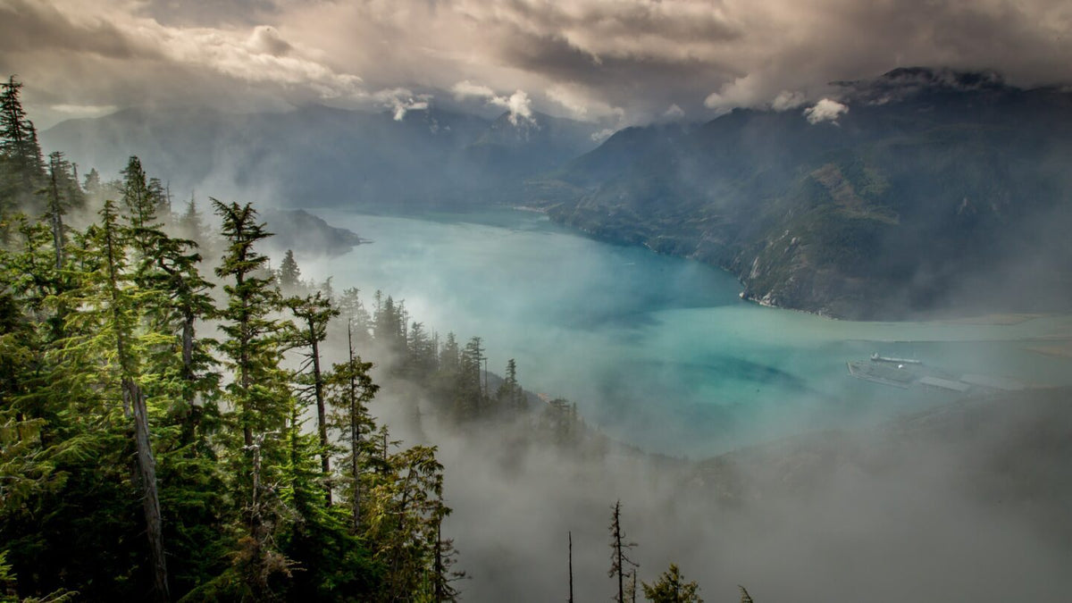 Low clouds over a turquoise mountain lake.