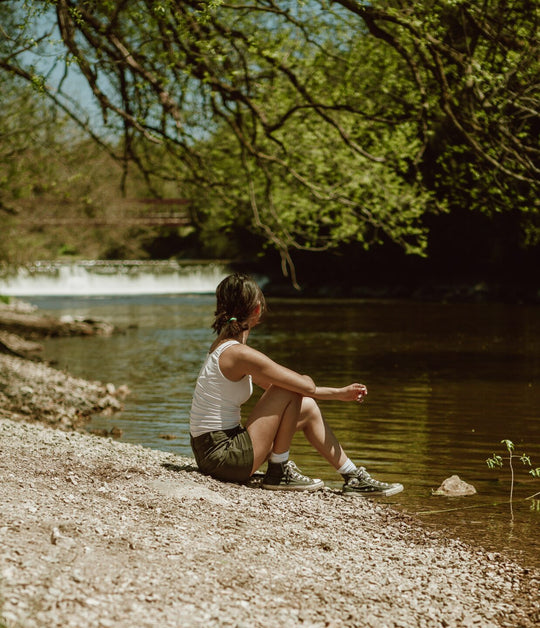 Woman sitting on a rocky shore overlooking a river.