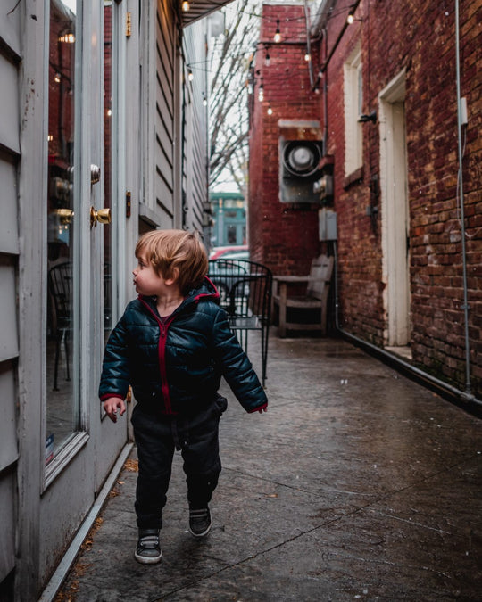 A toddler walking through a narrow urban alleyway lined with tall brick walls, exploring with curiosity