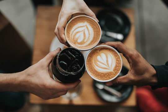 Three people clinking their drinks together at a cafe indoors.