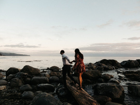 Man leading woman along rocky path to the water.