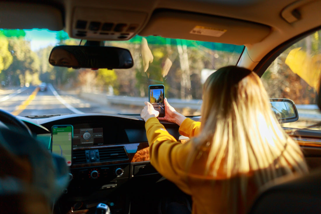 Woman taking a photo from the passenger seat of a car.