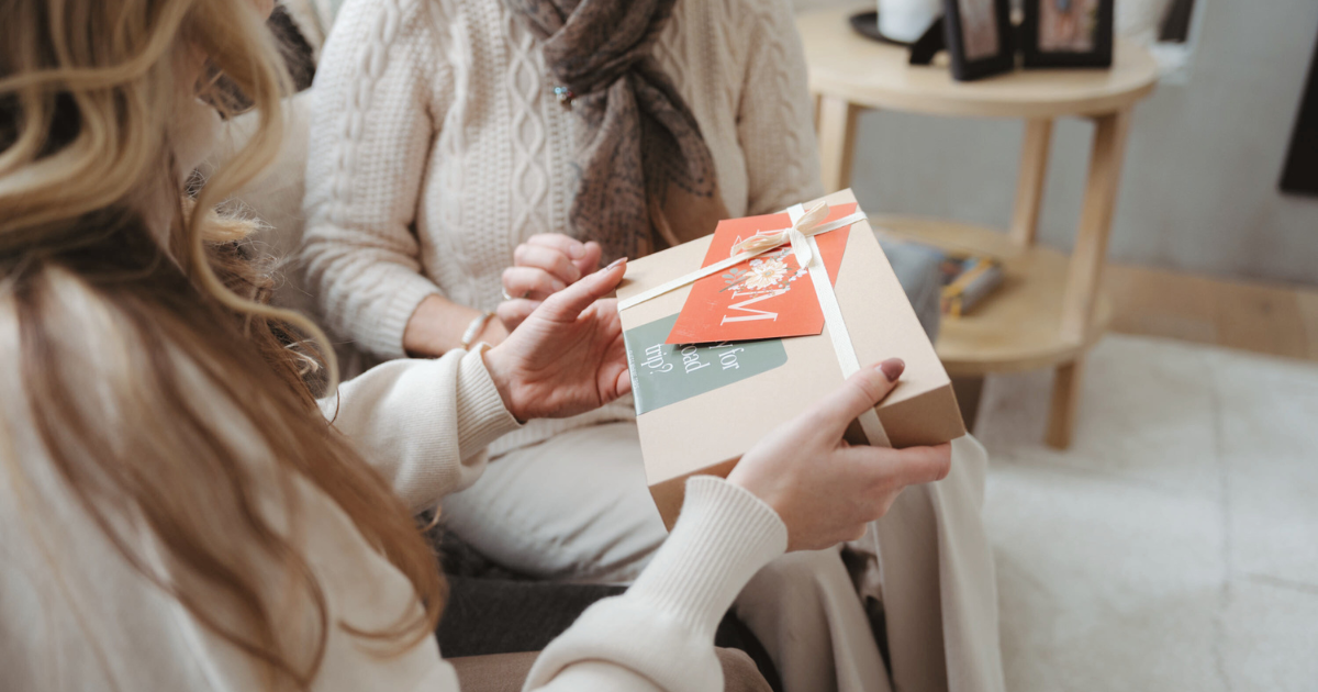 Daughter handing her mother a Guess Where Trips Mother's Day gift box.