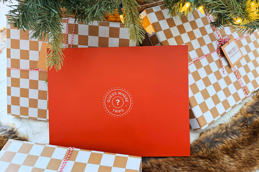 Red Guess Where Trips gift box underneath a christmas tree