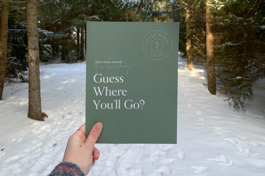 Woman holding green Guess Where Trips folder in front of a winter forest.