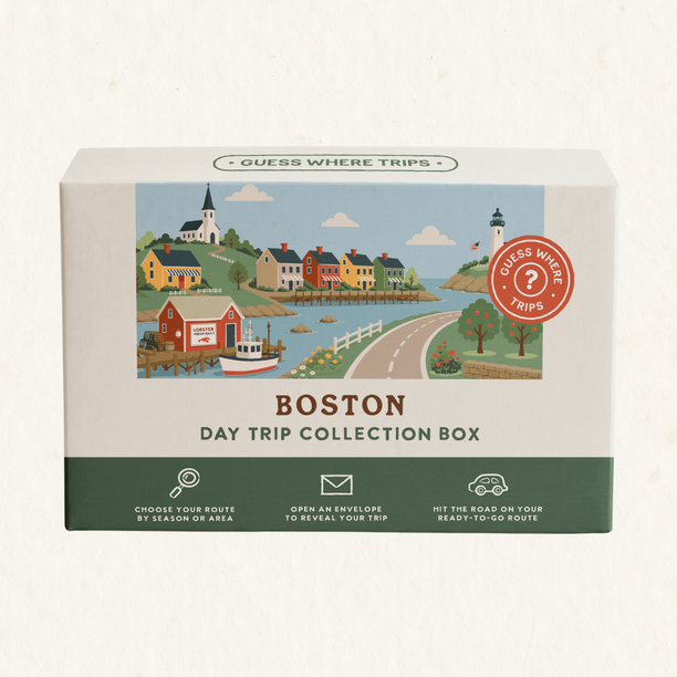 Boston Day Trip Box by Guess Where Trips, illustrated with a New England harbour village, a white church steeple, colourful houses and a lighthouse.