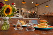 Bakery counter with sandwiches, cookies, and flowers on a wooden table.
