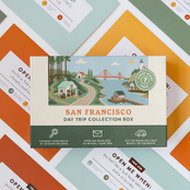 Bay Area Day Trip Box resting on a spread of colourful sealed trip envelopes.