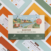 Boston Day Trip Box resting on a spread of colourful sealed trip envelopes.