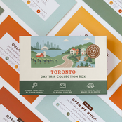 Toronto Day Trip Box resting on a spread of colourful sealed trip envelopes.