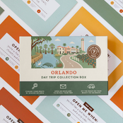 Orlando Day Trip Box resting on a spread of colourful sealed trip envelopes.